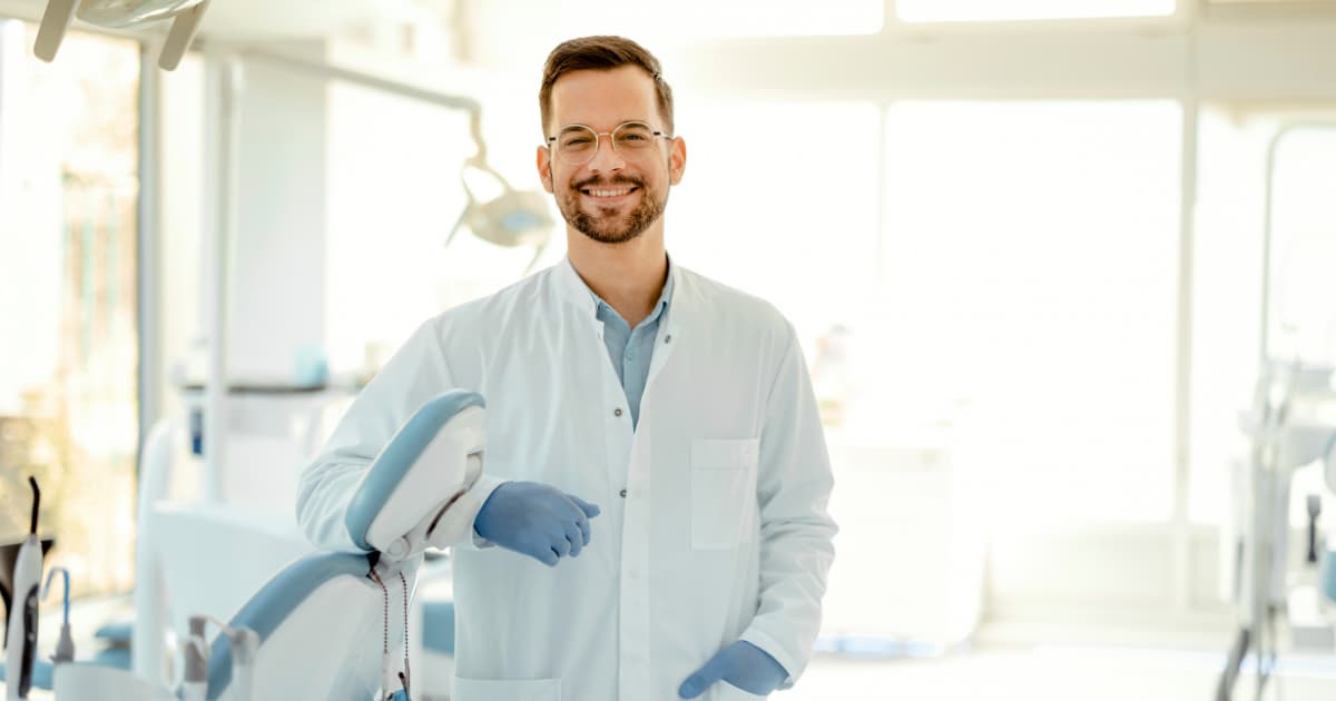 a dentist stands smiling by his dental chair.