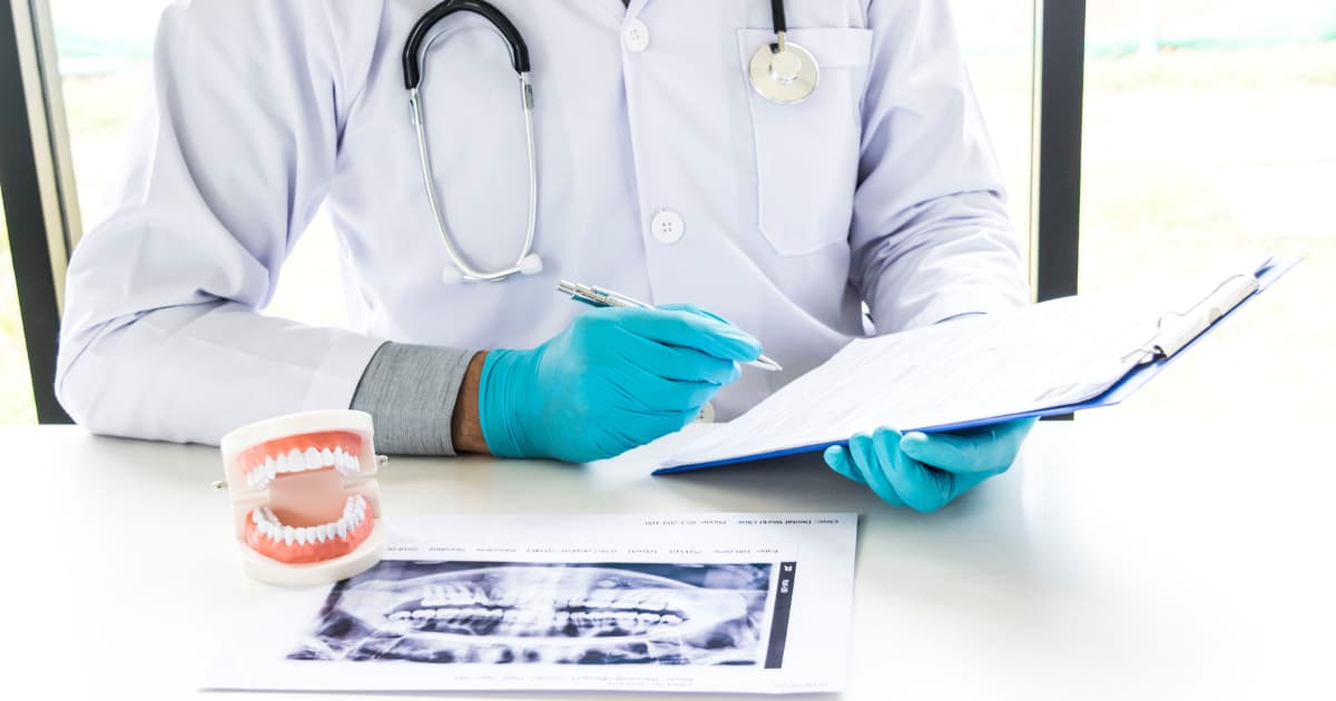 a dentist is sitting at a table with a clipboard, looking at a dental x-ray and a model of teeth
