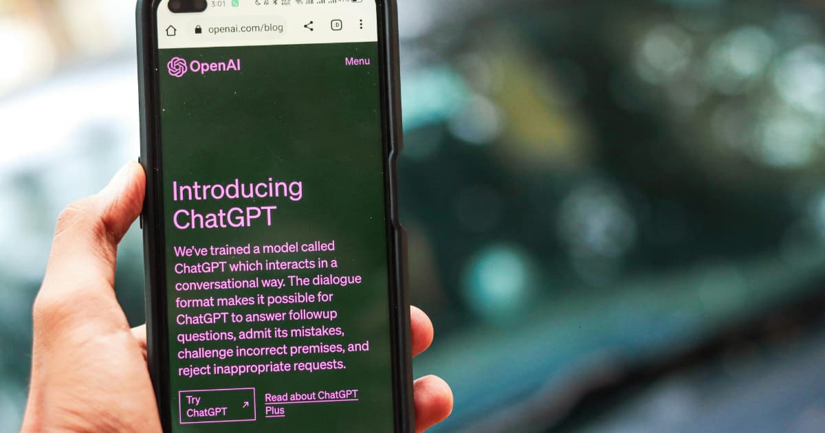 a hand holding a phone that shows OpenAI, Introducing ChatGPT text on the screen
