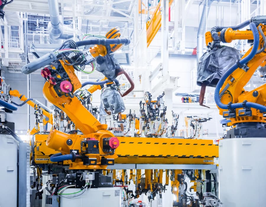 Two yellow industrial robotic arms operate on an automated manufacturing assembly line.