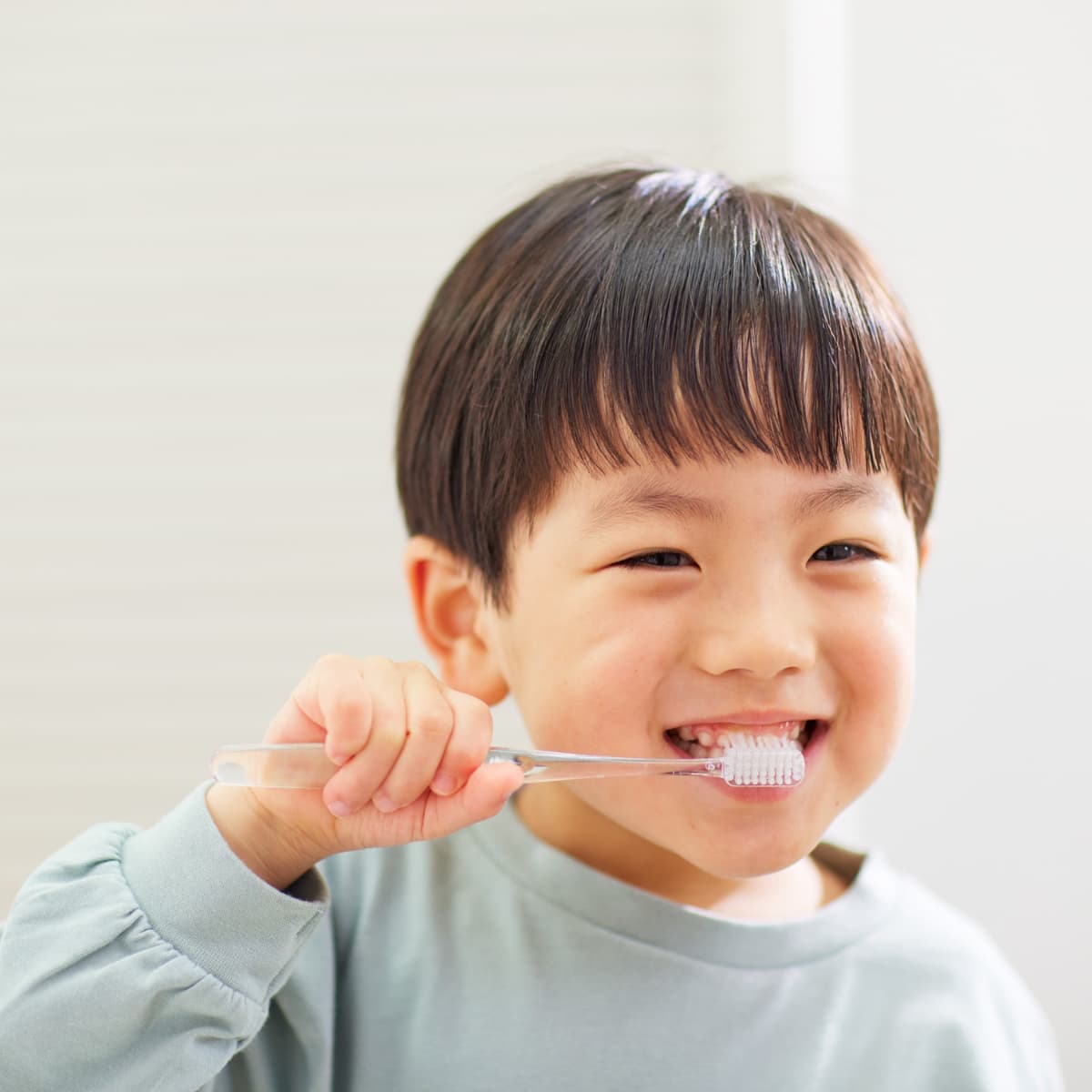 little boy wearing a gray shirt brushing his teeth